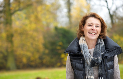 Smiling middle age woman standing in a park setting illustrating that therapy with Christina Winkler can help you achieve the feeling of calm and equilibrium you need.
