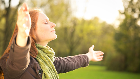 Image of a smiling young woman with eyes closed and arms out wide facing the sun, illustrating that Gestalt therapy is about creating real and meaningful change.