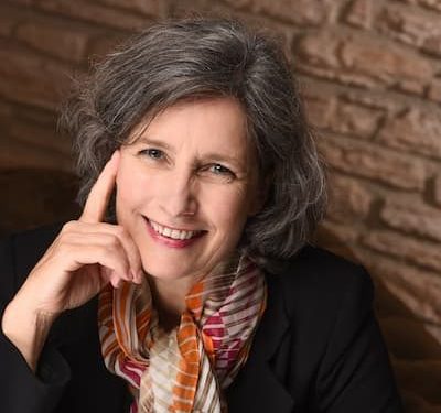Indoor headshot of Christina Winkler smiling with her hand against the side of her face, illustrating that Christina Winkler gives people space to make meaningful and lasting improvements in their lives.