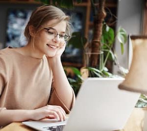 Smiling young woman sitting in front of a laptop, illustrating that Christina Winkler offers accessible online therapy appointments.