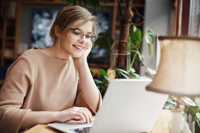 Young smiling woman sitting at a desk in front of her laptop, illustrating that Christina Winkler provides online therapy to meet your needs.