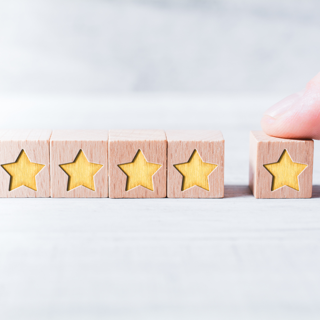 Image of a hand pushing a fifth wooden cube with a golden star into a row of four other cubes, each also topped with a golden star, symbolizing a five-star rating.